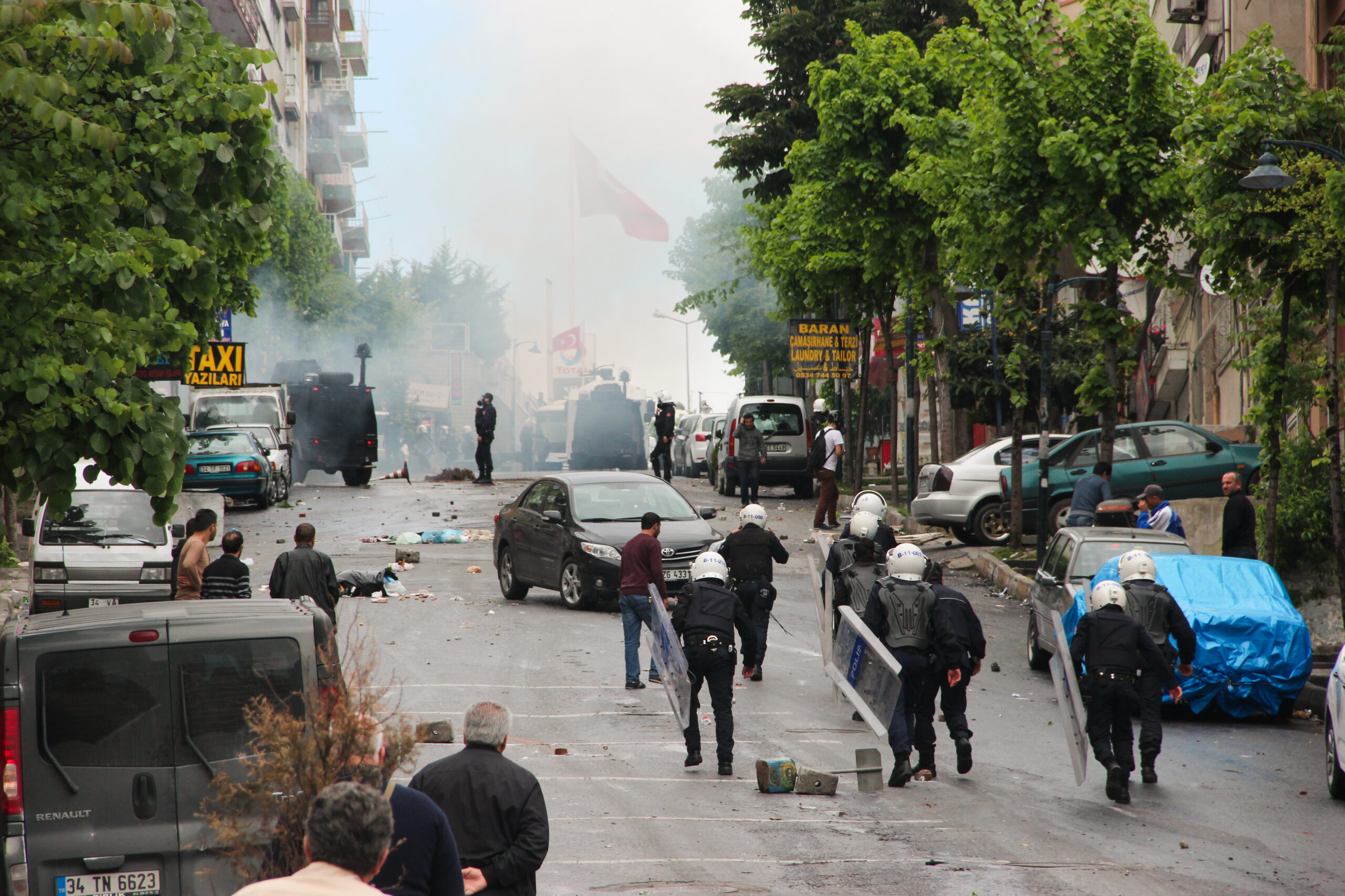 Riot police on a hilly street in Istanbul dispersing protesters. The street is full of debris and smoke can be seen in the background.