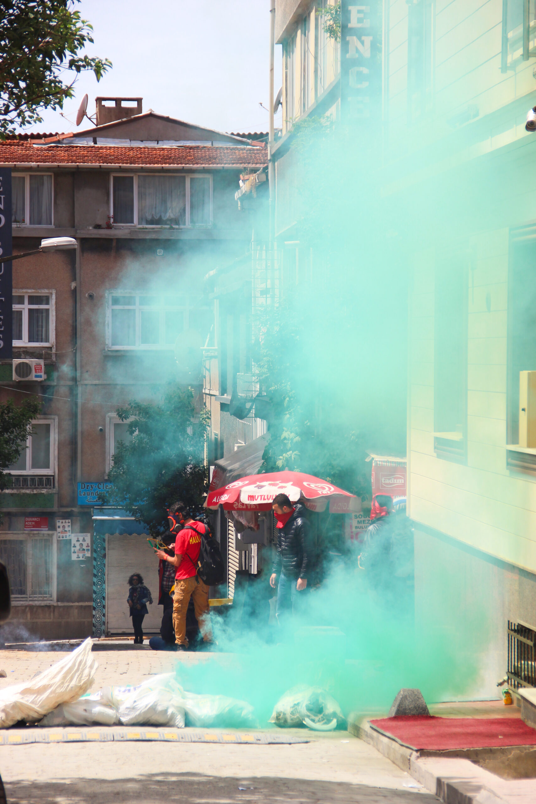 Protestors with face coverings stand in a street in Istanbul filled with teal coloured gas.