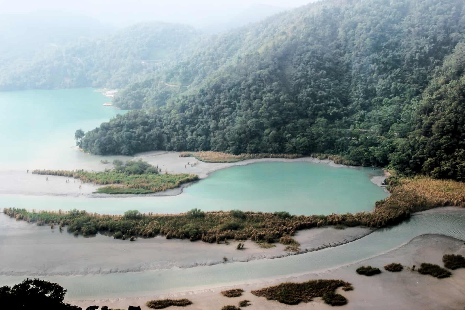A turquoise-blue-green cove backed by a mound of forest on a corner of Sun Moon Lake. 