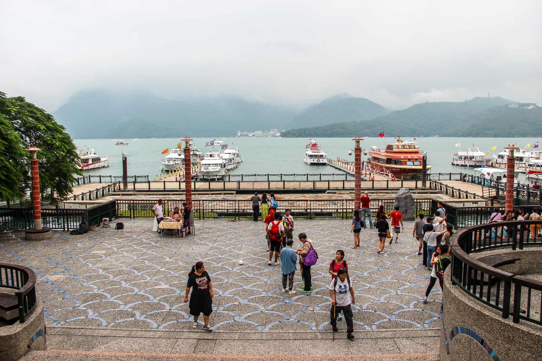 Boat dock and visitors at a pier at Sun Moon Lake in Taiwan, backed by mountains.