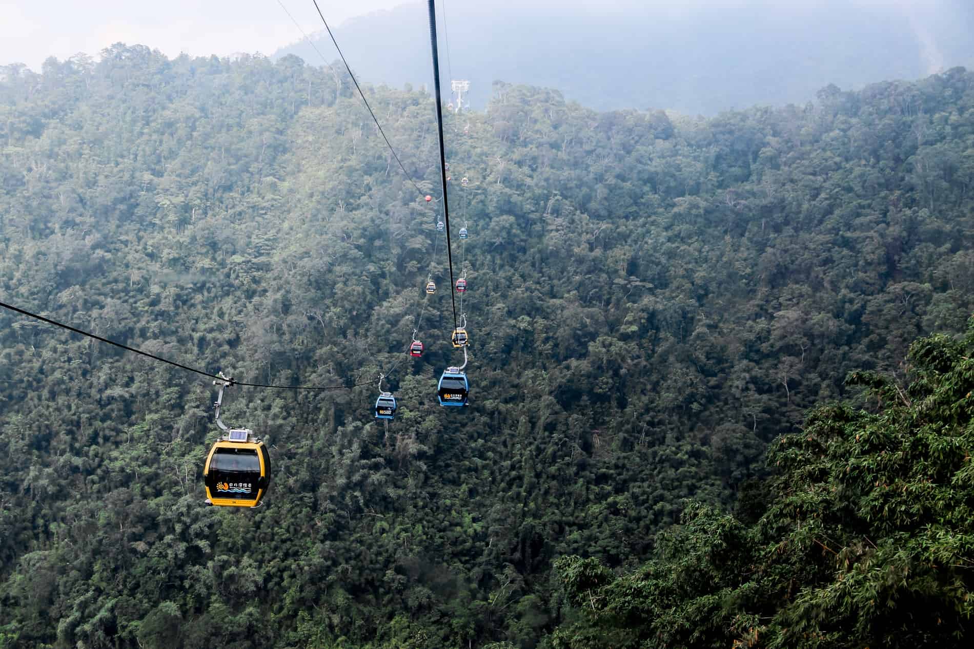Yellow, blue and red gondola cars travelling over the thick forest of the Sun Moon Lake mountains in Taiwan. 