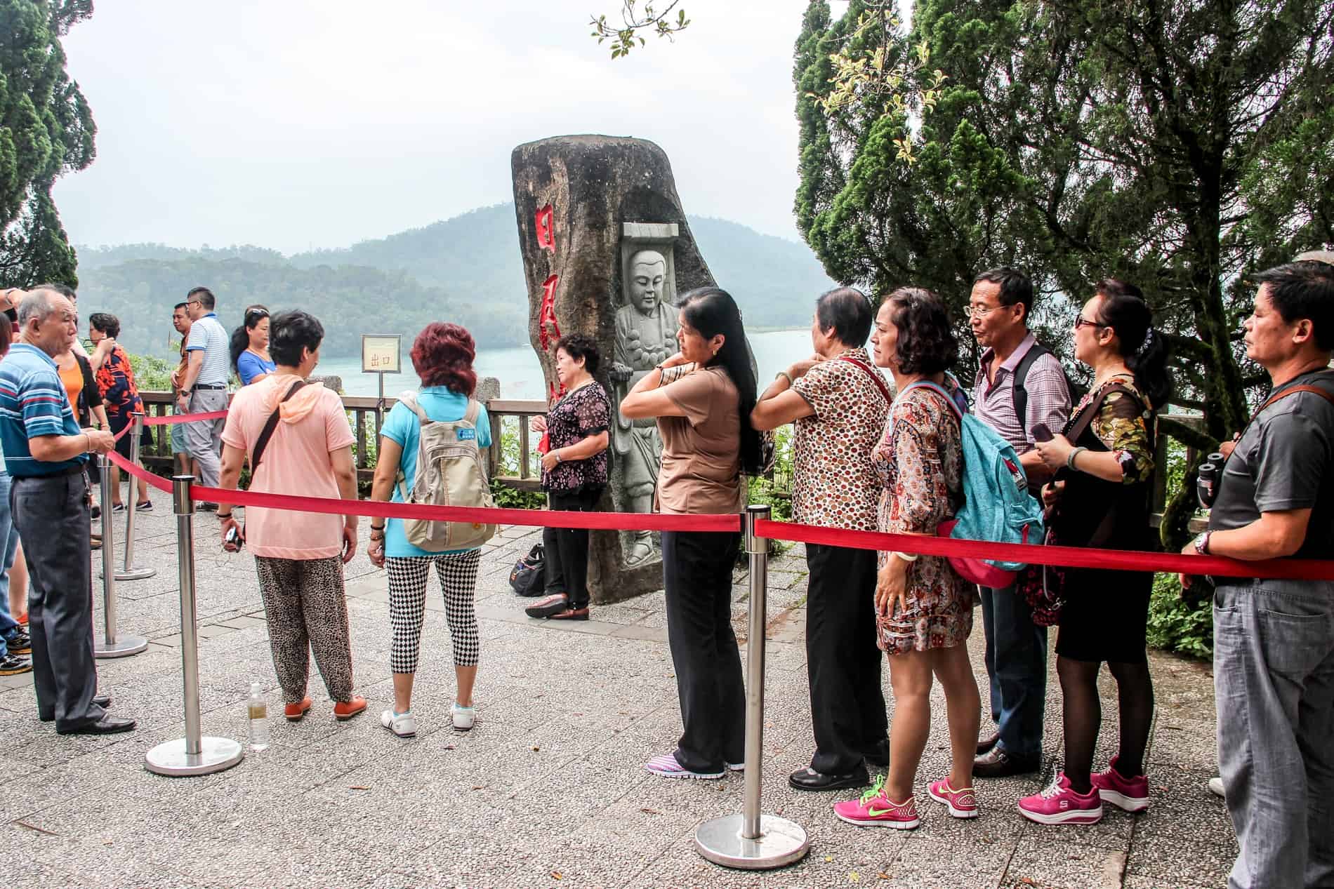 People queue around a stone carved with a relief of a religious figure, at an elevated spot overlooking Sun Moon Lake. 