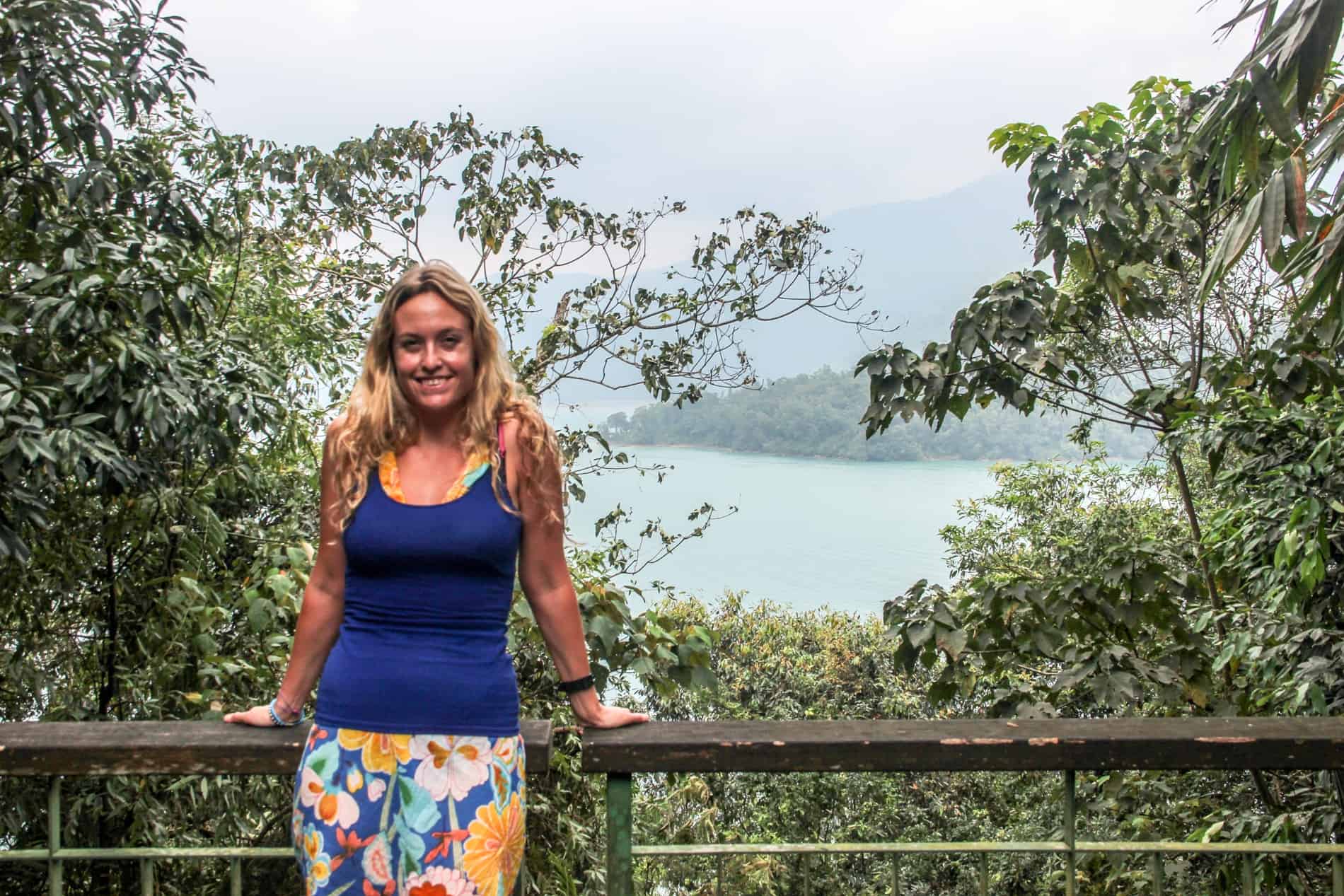 A woman leans on a wooden rail at an elevated viewpoint overlooking the huge Sun Moon Lake in Taiwan. 