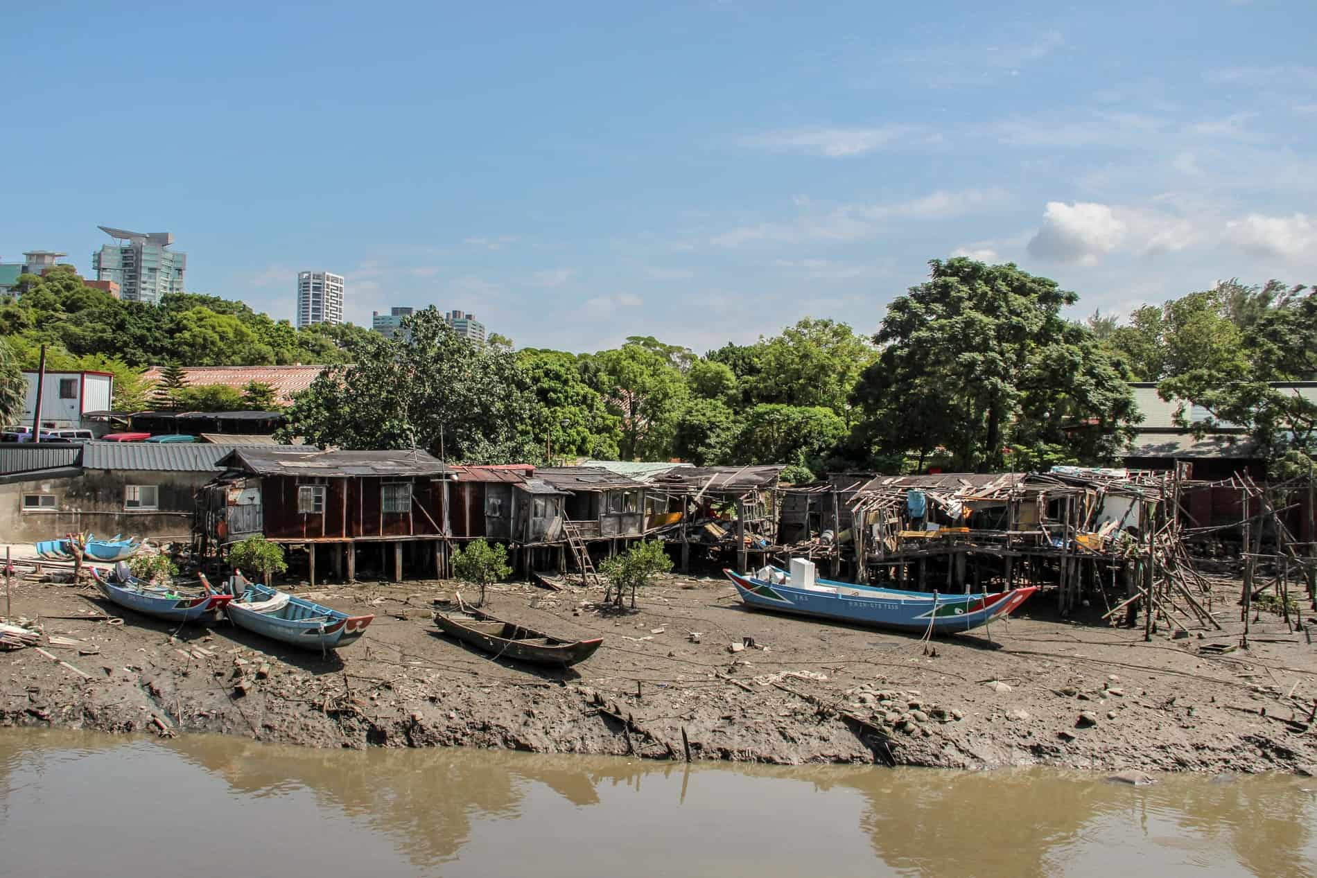 Stilt houses and boats sit on muddy earth along the Tamsui River in New Taipei.
