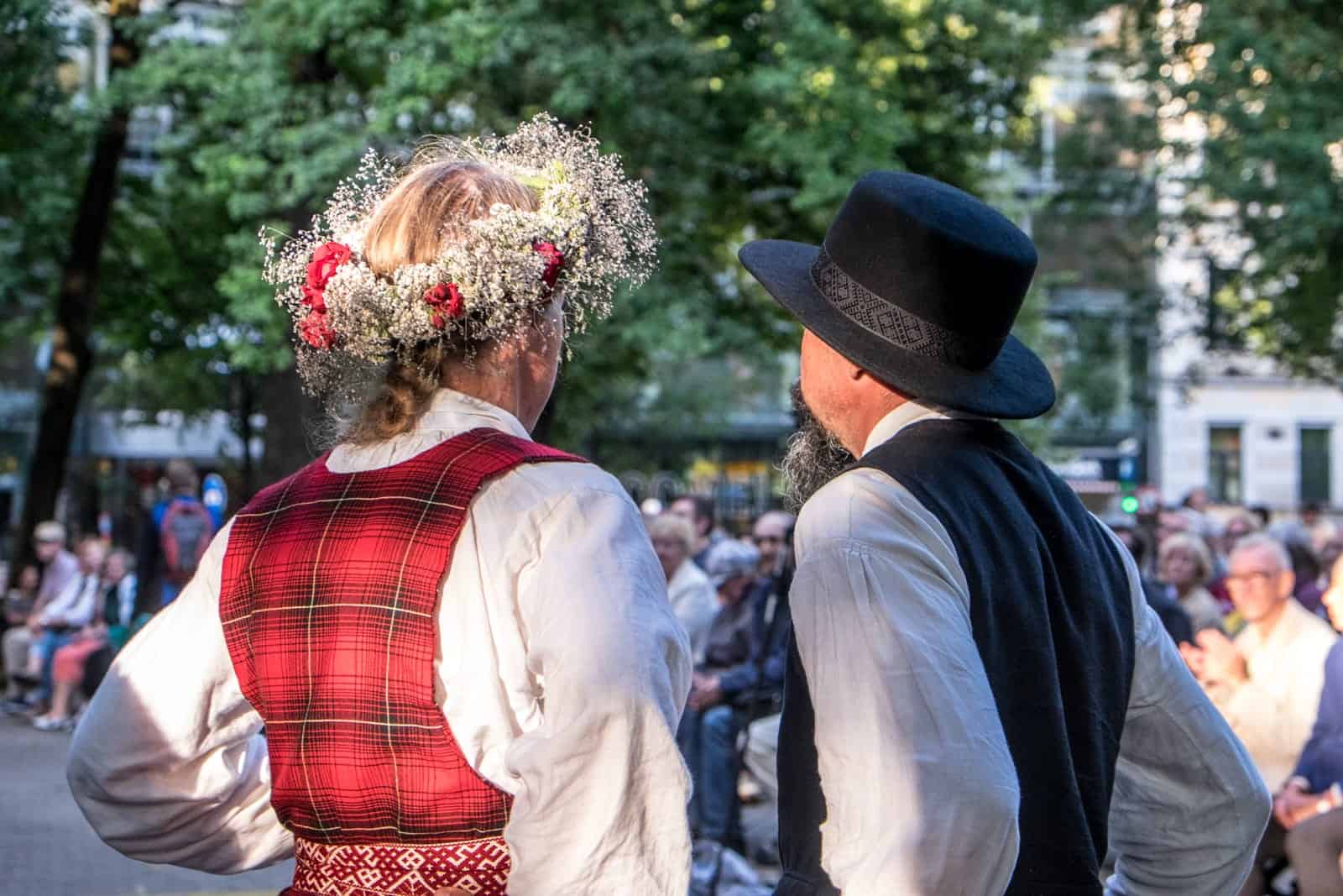 Two people wearing folk costume watching a performance at the Song and Dance Celebration in Latvia