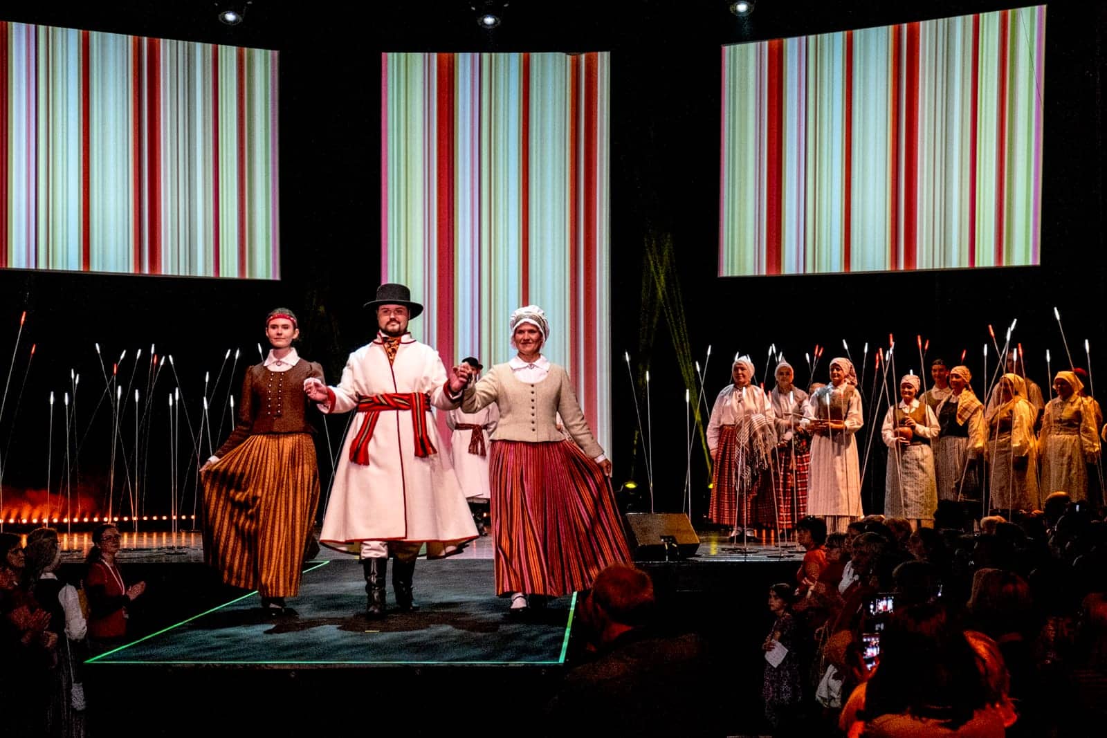 A man and two women showing designs at Folk costume catwalk show in Riga for the Song and Dance Celebration in Latvia