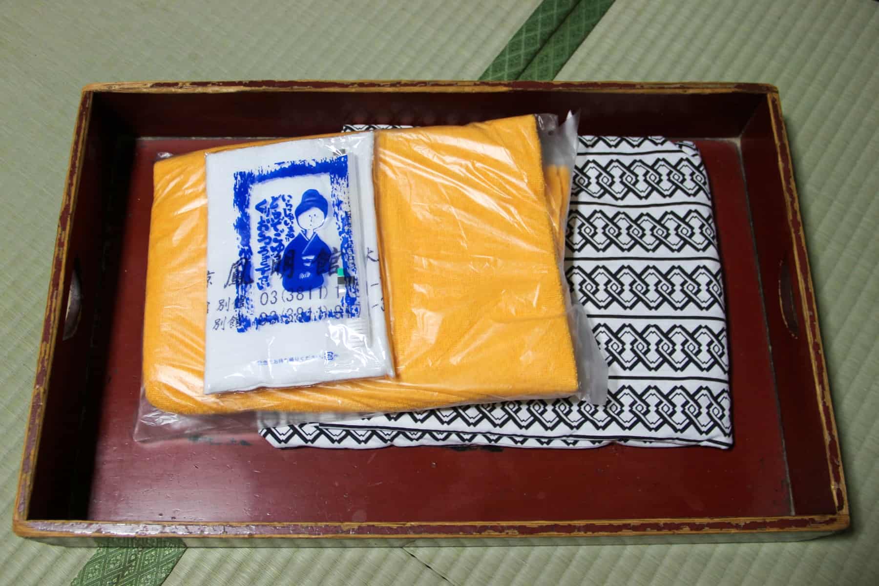 A wooden tray in a Japanese Ryokan room containing a Yukata bathrobe and packaged yellow and white towels.