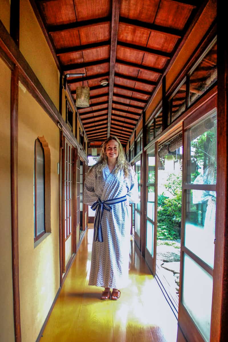 A woman wearing a white and blue Yukata bath robe in a wooden corridor of a Japanese Ryokan in Tokyo. 