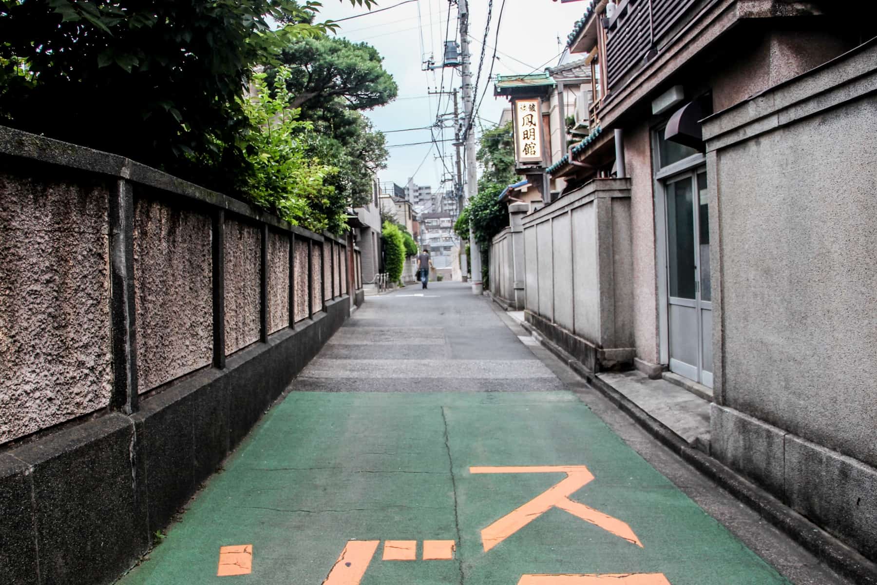 A quiet residential street on a Tokyo neighbourhood with the street name in yellow writing on a green painted path. 