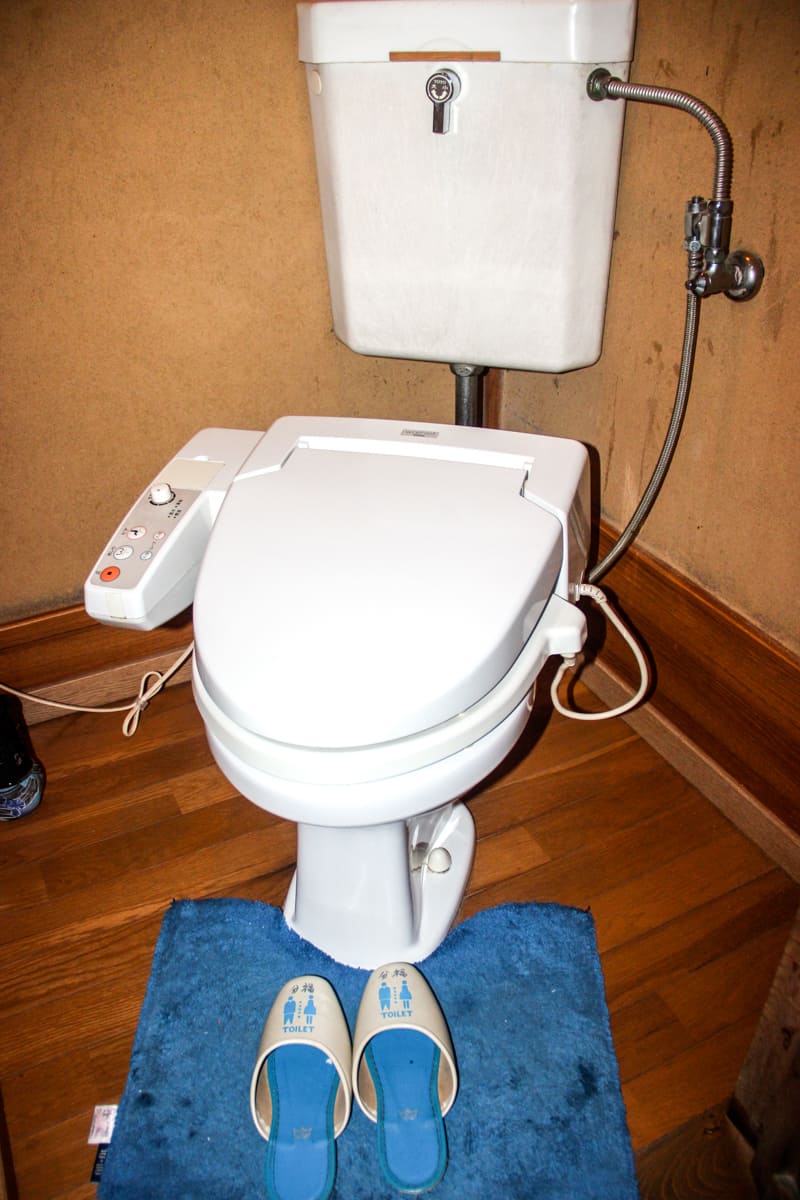 A white Japanese toilet with buttons and a pair of toilet slippers in an old Japanese Ryokan in Tokyo. 