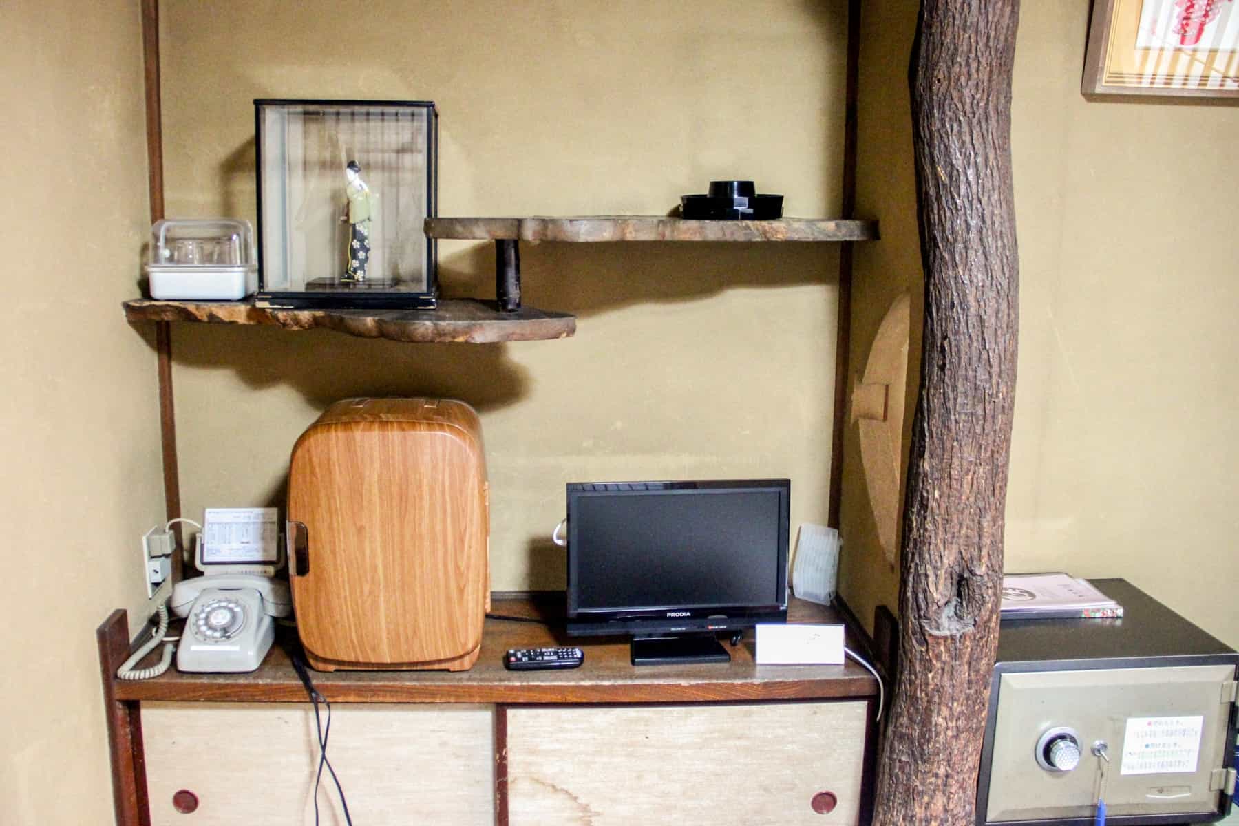 Wooden shelving with a phone, fridge, TV and safe - amenities in a room at a Japanese Ryokan. 