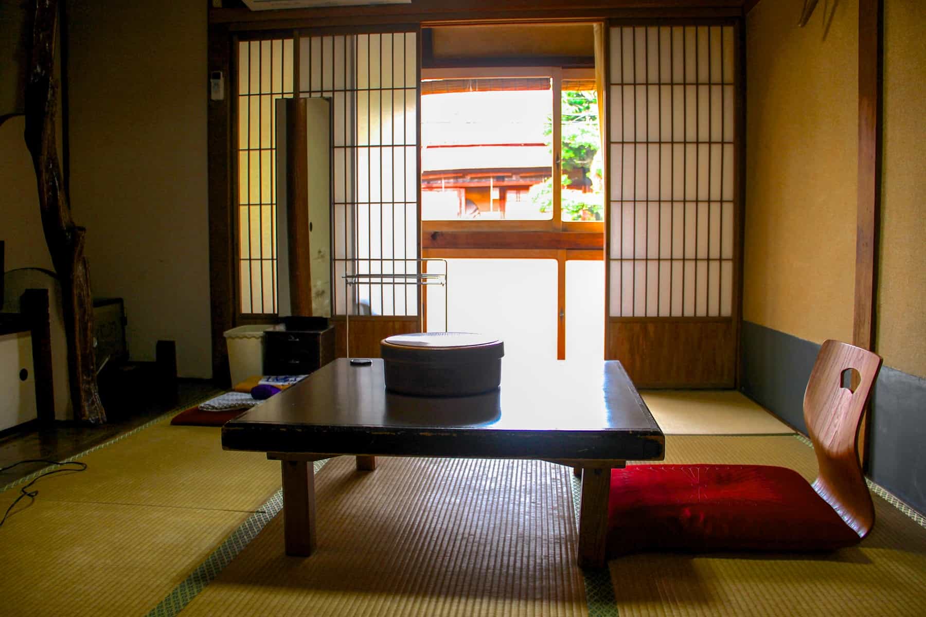 A room in a traditional Japanese Ryokan with wooden sliding doors, a wooden, floor chair and reed mat.