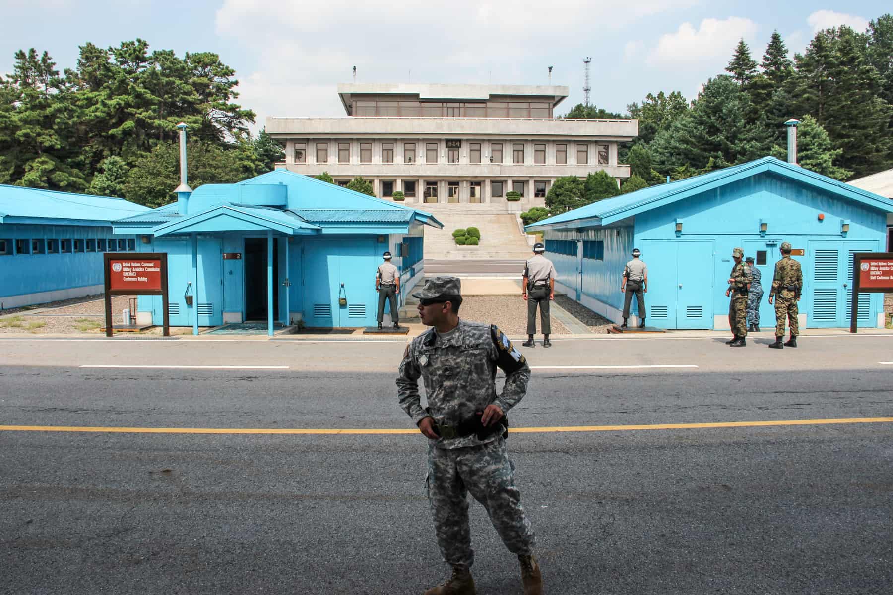 An American military man at Joint Security Area stands on front of three South Korean guards and the America military at the blue buildings on the Demarcation line of the two Koreas. 