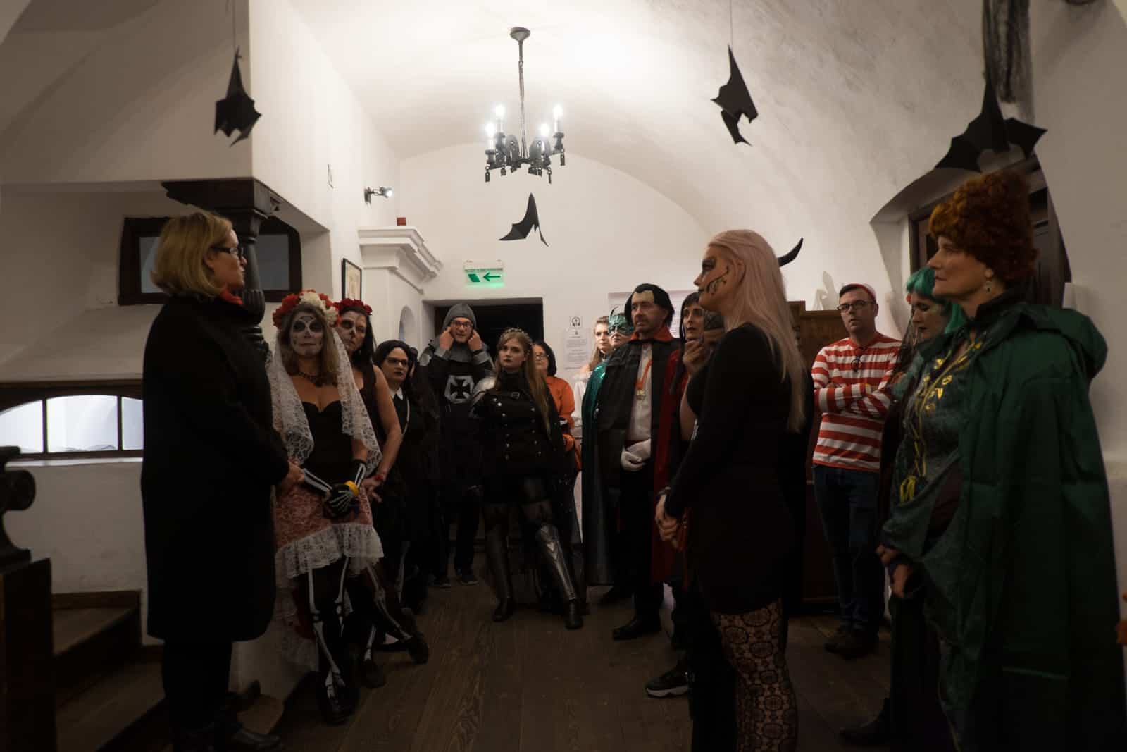 A group of people in Halloween costume listening to a female guide on a tour inside Bran Castle in Transylvania