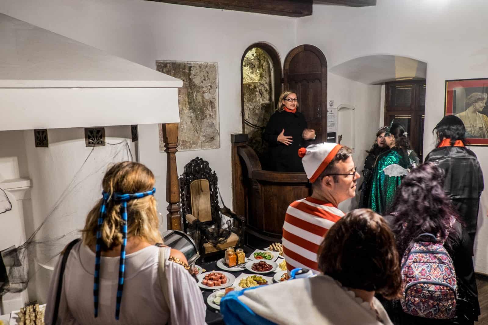 Seven people in Halloween costume follow a female guide through a room at Bran Castle, Transylvania, Romania