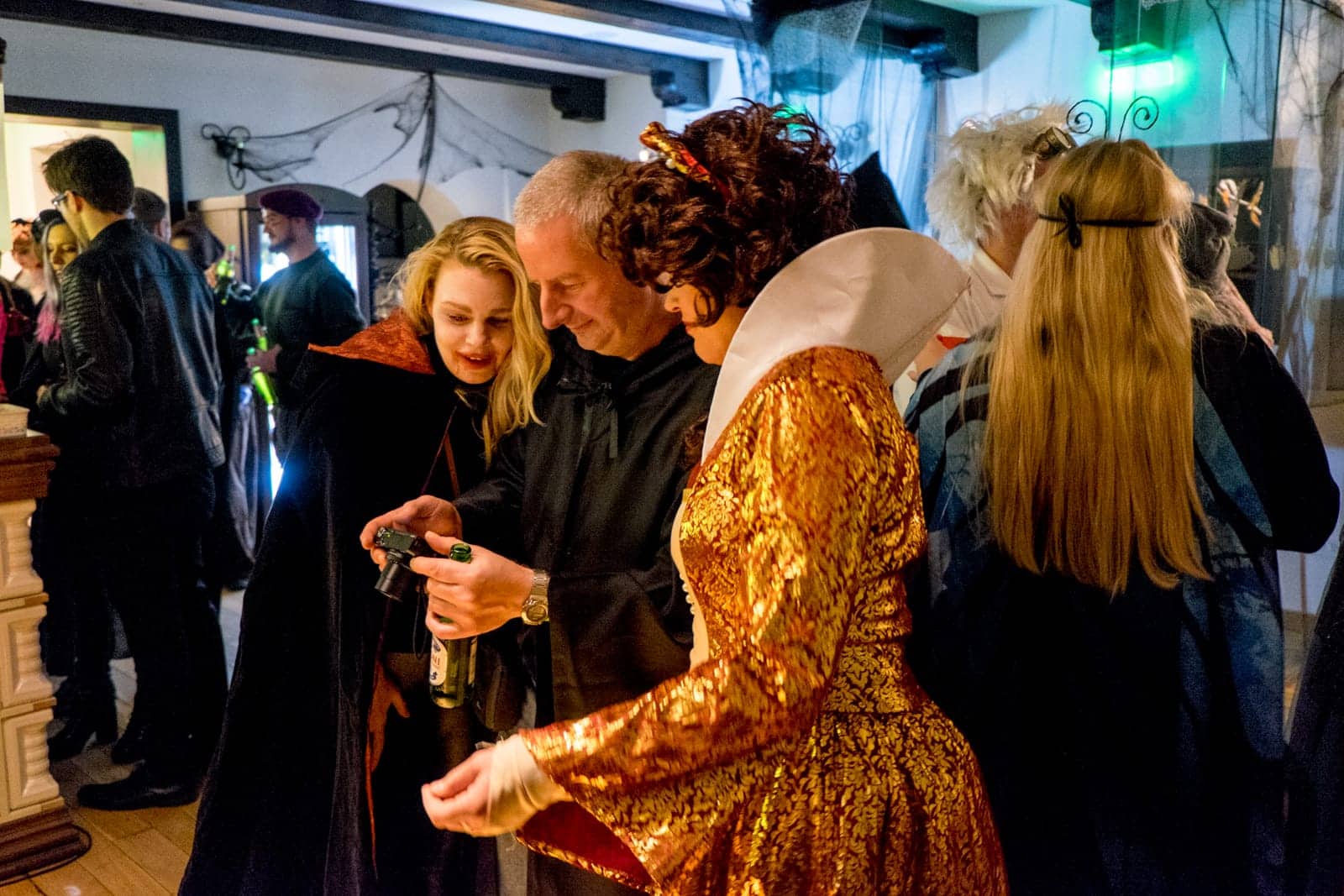 Three people dressed in Halloween costume check a picture of a small camera at a party in Bran Castle, Transylvania, Romania