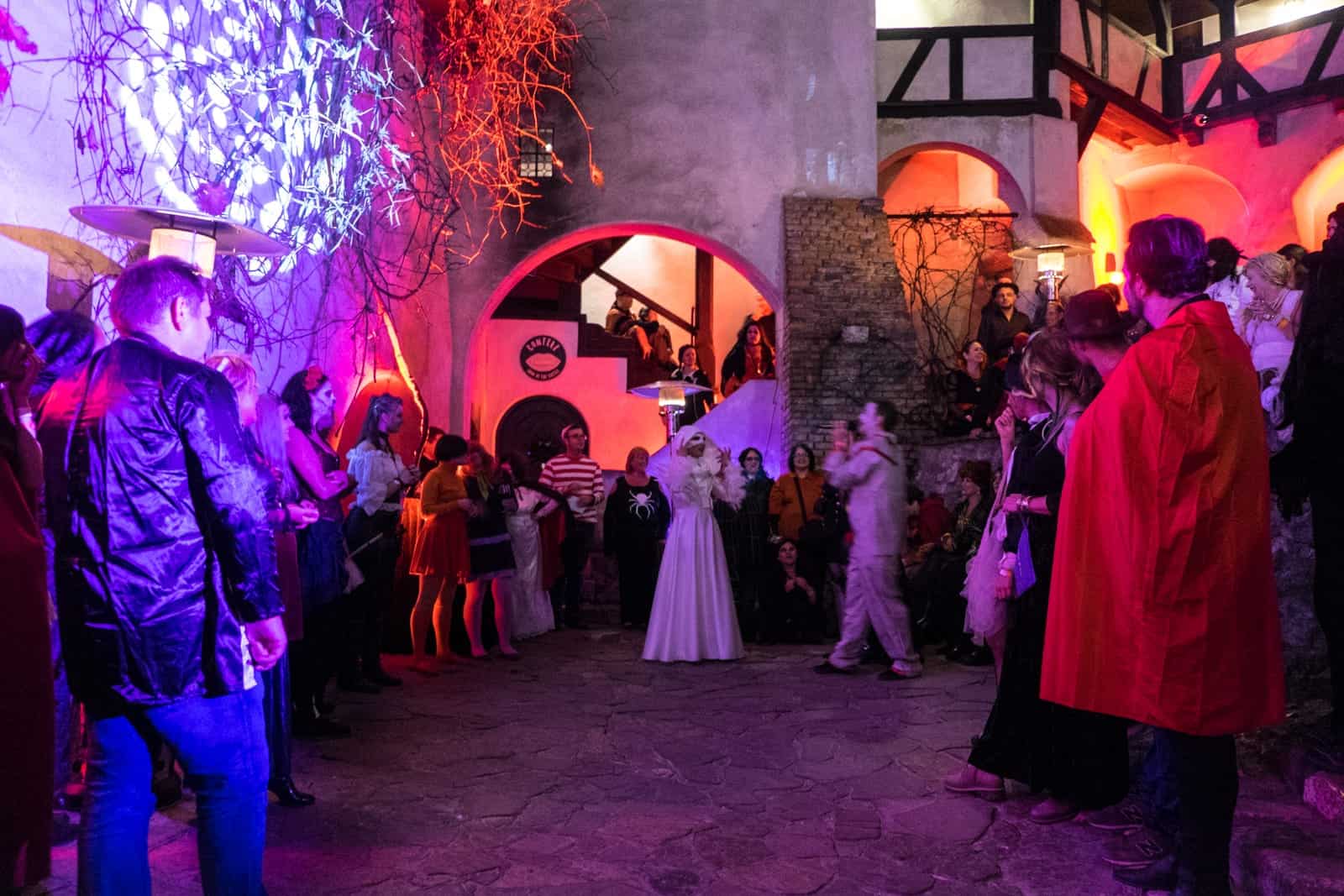 A group of people in Halloween costume form a wide circle in a courtyard in Bran Castle, Transylvania, Romania