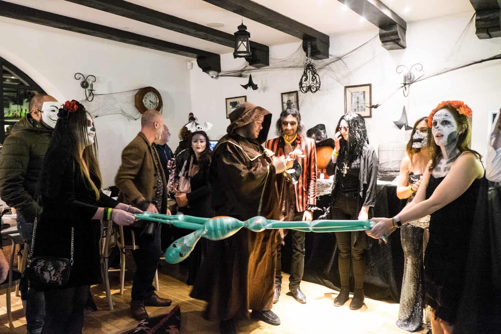 A group of people in costume, pulling a green inflatable alien at a Halloween party inside the white walls and dark beam roofed room at Bran Castle. 