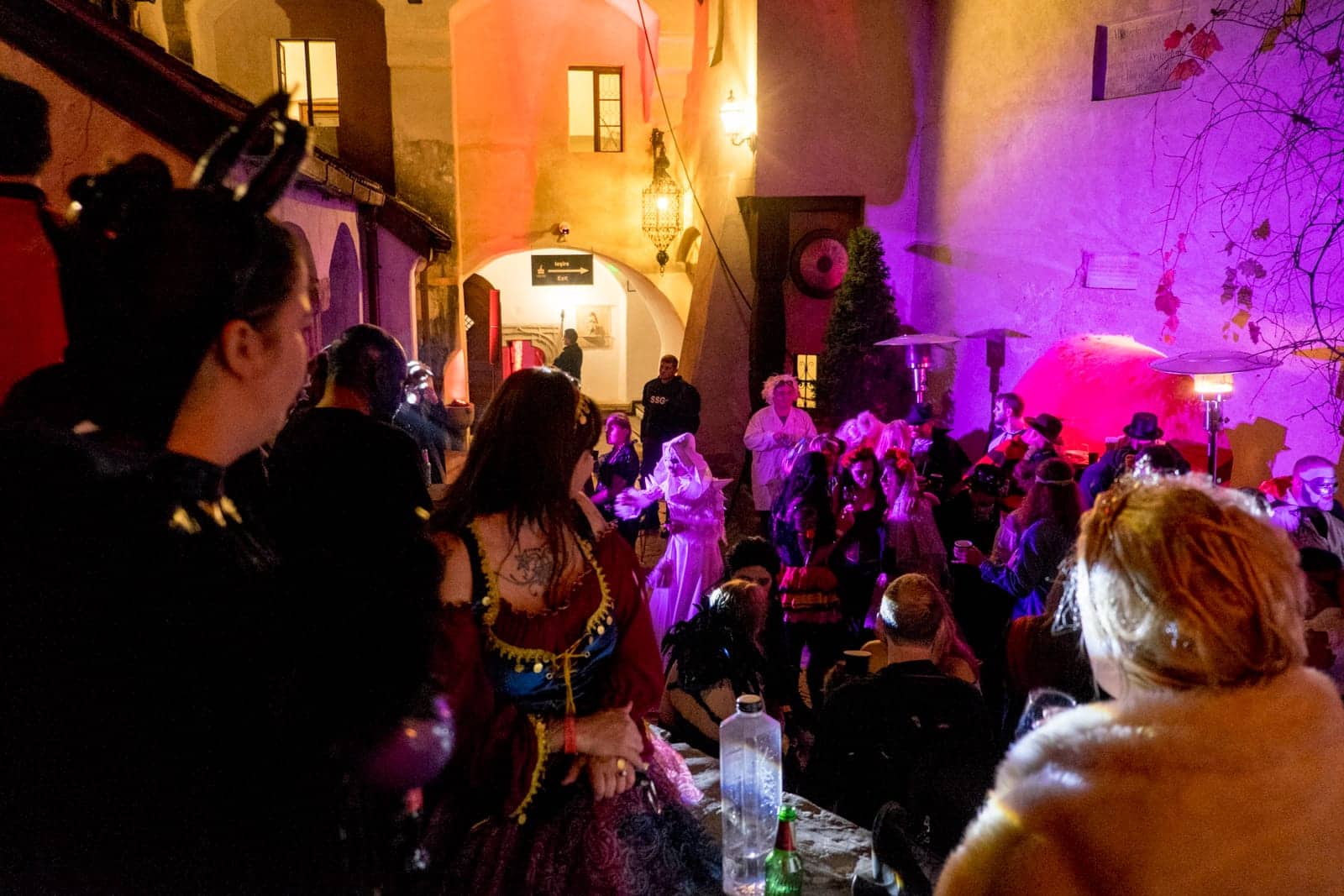 Three women dressed in Halloween costumes look towards fellow partygoers on the dance floor in a courtyard of Bran Castle, Transylvania, Romania