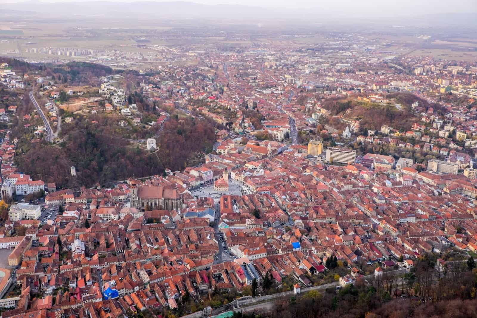 Elevated views of Brasov, Romania after hiking Tampa Mountain showing a mass of terracotta red houses and two circular patches of forest