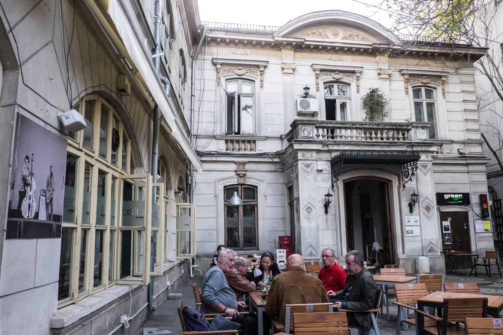 A group of people sit at a table within a classical, white marble stoned dining in a courtyard in Bucharest, Romania