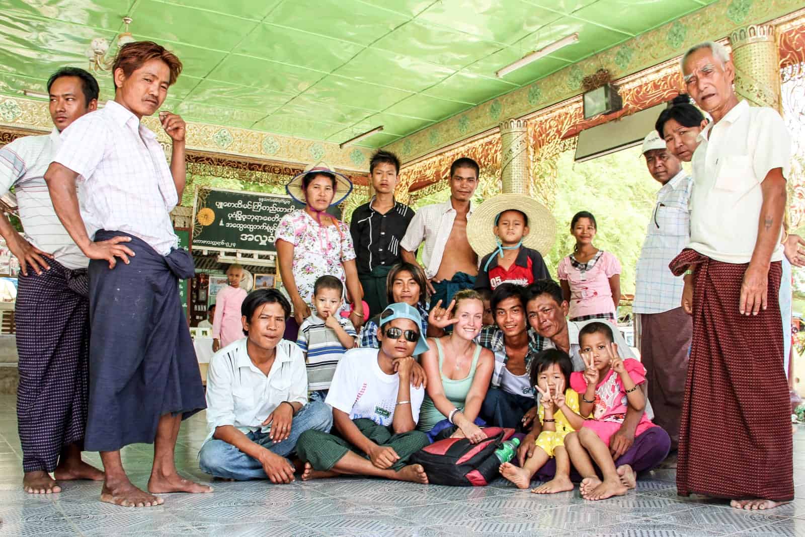 A woman in a mint green top sits on the floor on a green temple room surrounded by a group of Burmese people. Two men stand on the left, and two men and one woman are standing on the right. 