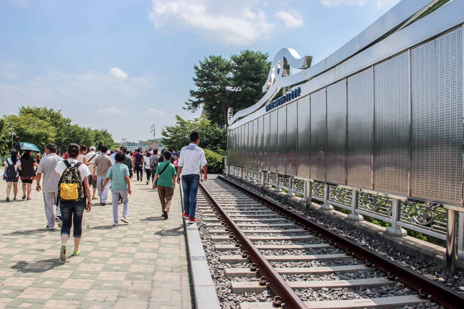A group of people walk past the railway track metal memorial inscribed with names at the Dorasan Train Station site during a DMZ visit. 