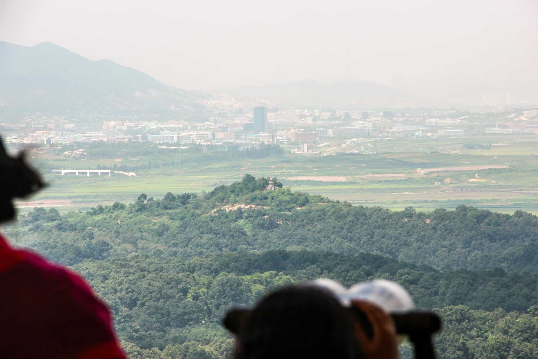 A view past the binoculars towards a green mound and the 'Propaganda Village' in North Korea, seen on a trip to the DMZ.