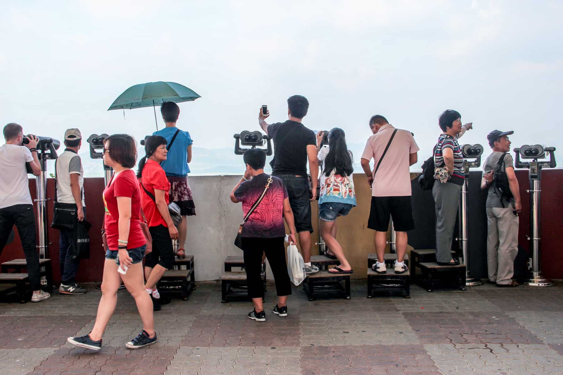 Visitors on a DMZ tour in South Korea at an observatory with rows of binoculars looking out to North Korea.
