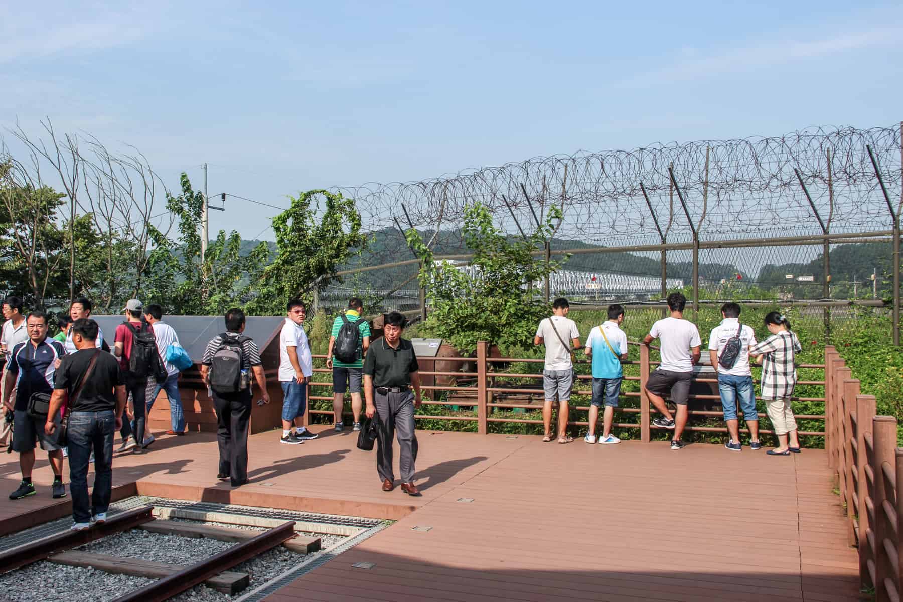Travellers on a DMZ tour at the site of an unused section of a railway line intended to connect South and North Korea. Beyond the fence and barbed wire is a view to the white Friendship Bridge meant to unite the two countries. 