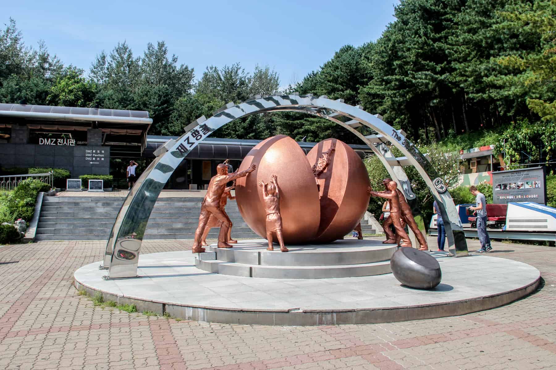 A golden bronze artwork depicting people pushing two halves of a sphere together for reunification, marks the entrance of the Third Infiltration escape Tunnel at the DMZ in South Korea.