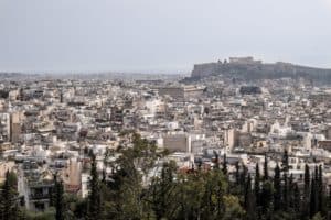 Elevated view over the densely packed buildings of Athens city in front of the Acropolis hill, with the Parthenon structure on top.