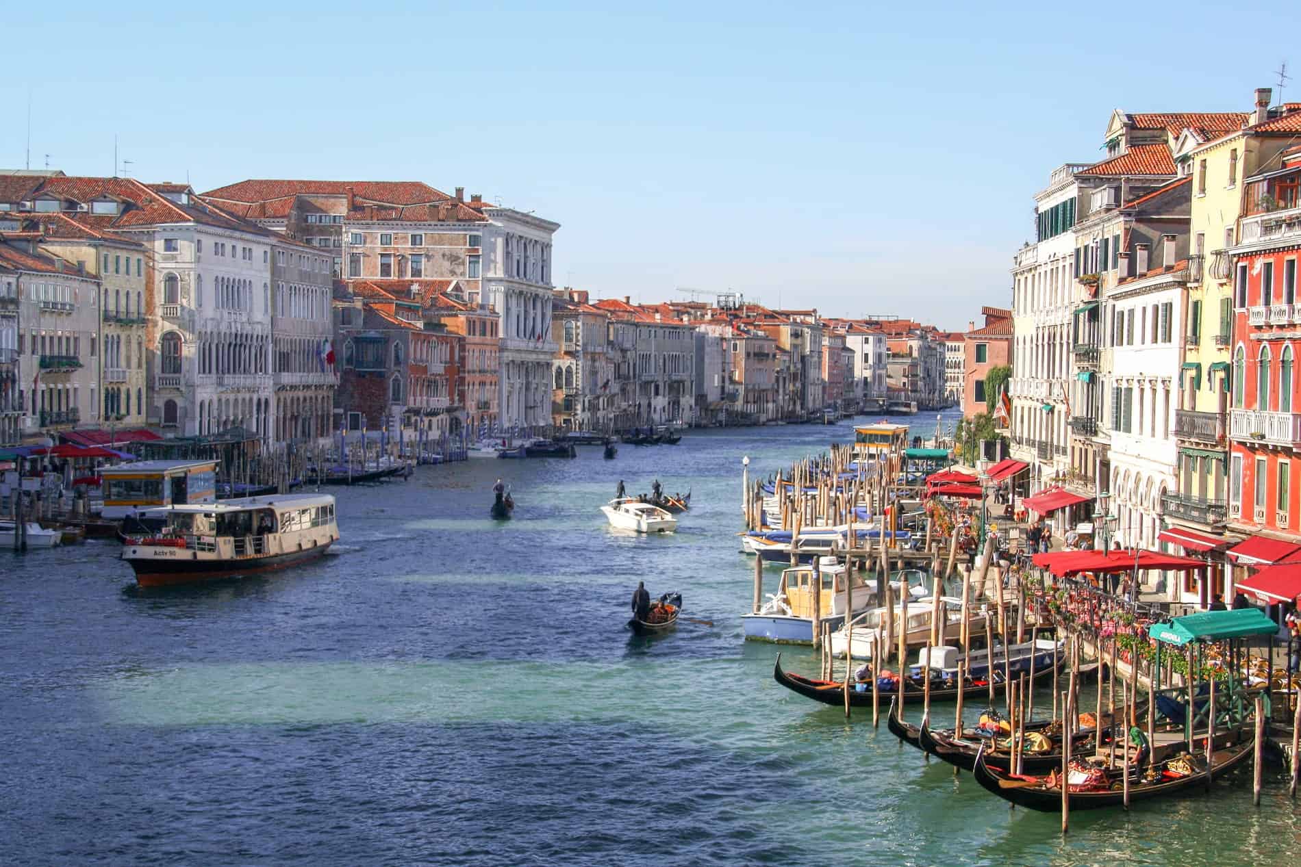 Elevated view of the wide boat-filled Grand Canal in Venice lined with tall, colourful buildings.
