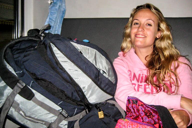 A woman in a pink hoodie sitting next to a large backpack on a night train seat in Southeast Asia. 