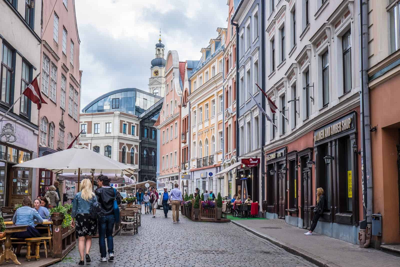 Pastel hued building facades on a wide cobblestone street in Riga Old Town.