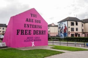 A pink painted exterior house wall displaying the words 'You are Now Entering Free Derry Corner'.