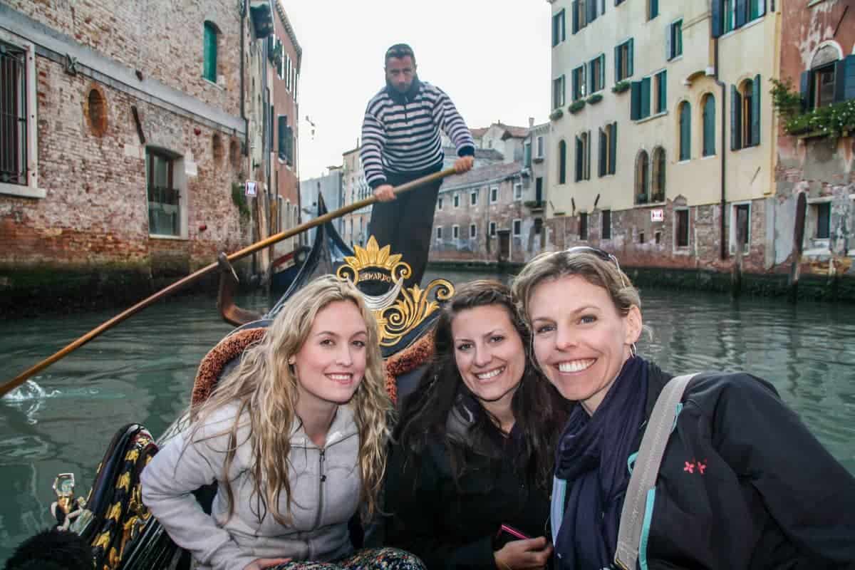 Three tourists on a gondola ride in Venice, with the Gondolier steering it behind them