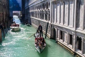Tourists on a gondola ride in Venice travelling down a narrow canal of aqua water