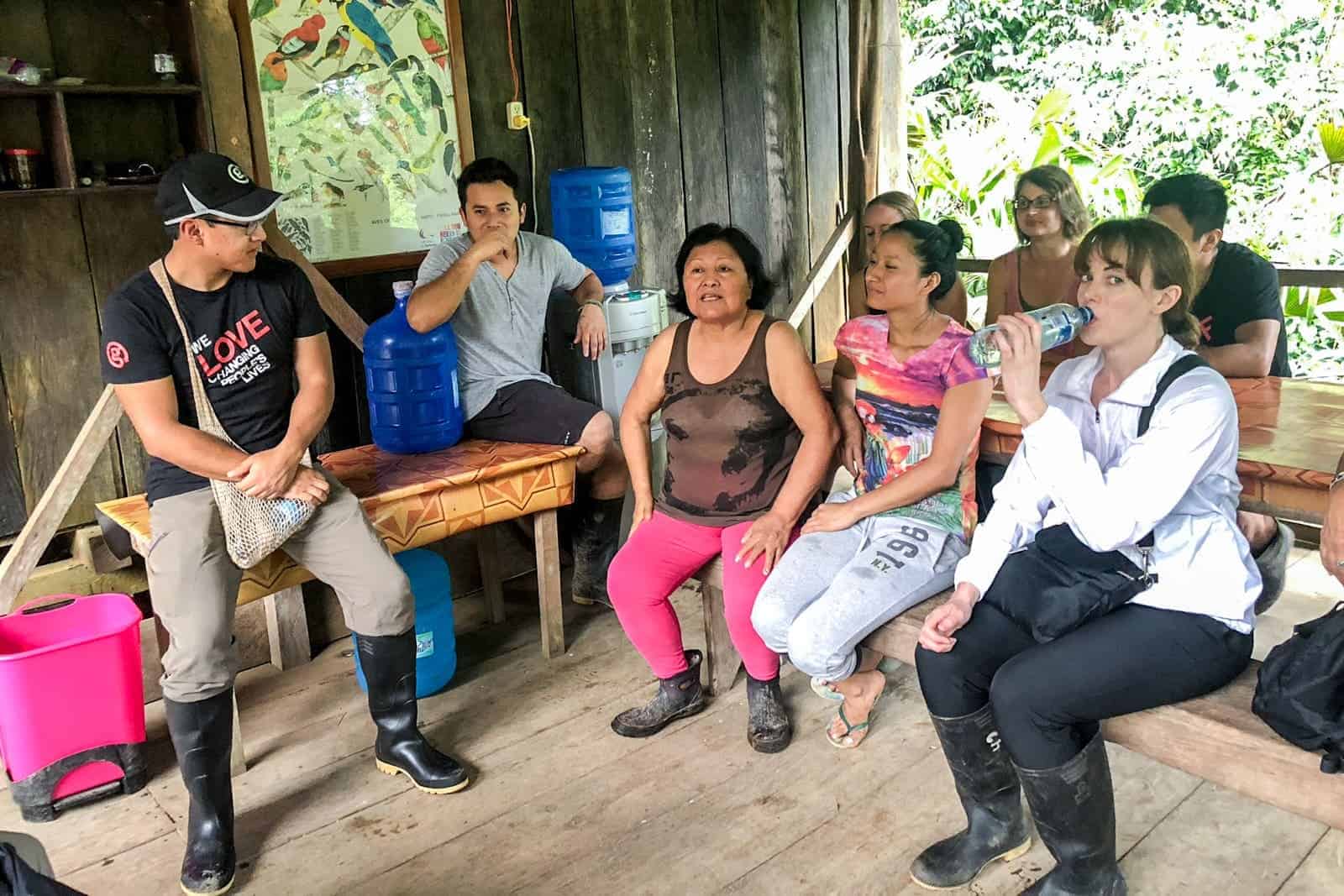 A group of travellers sitting in a wooden house, conversing with a local family living in the Ecuador Amazon.