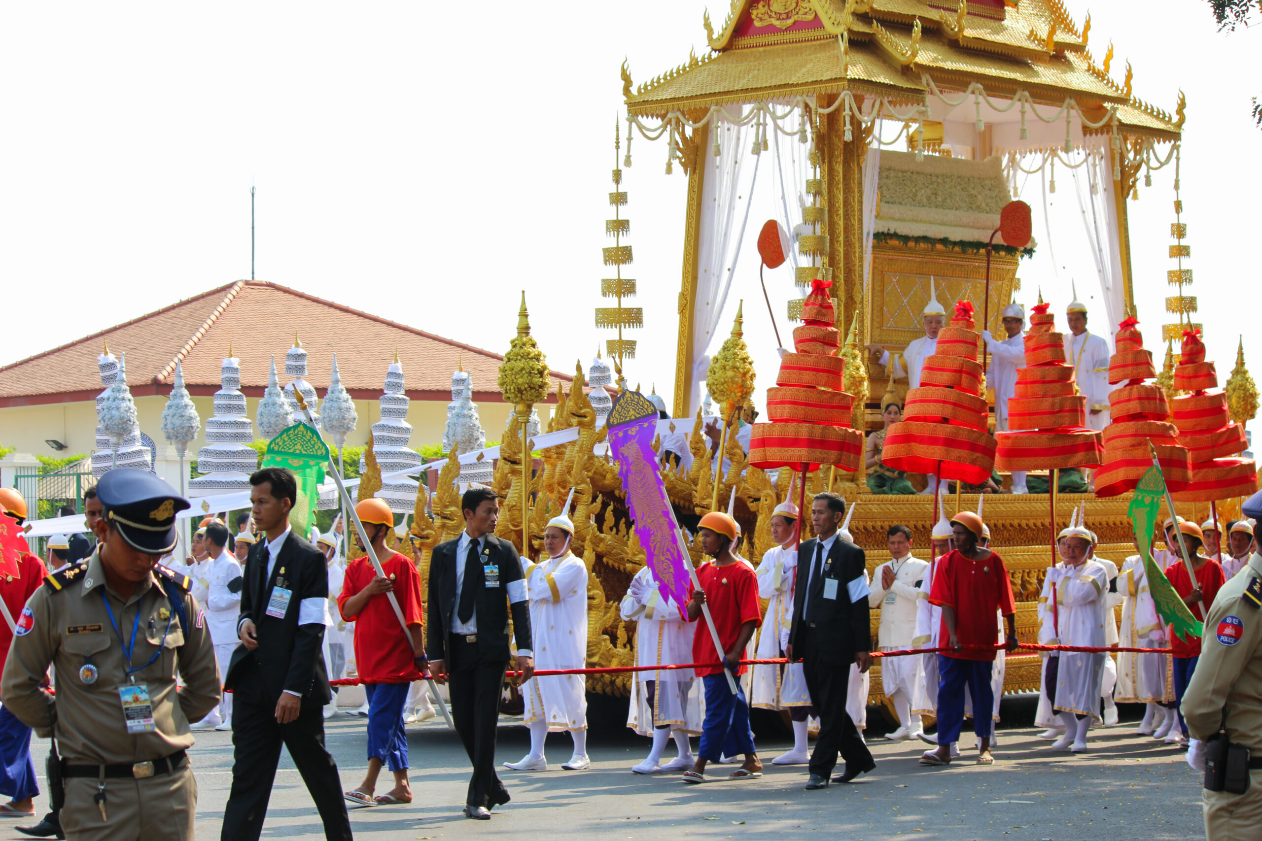 A group of people dressed in white walking alongside a grand golden float topped with the golden coffin sarcophagus of Norodom Sihanouk during his state funeral in Cambodia.