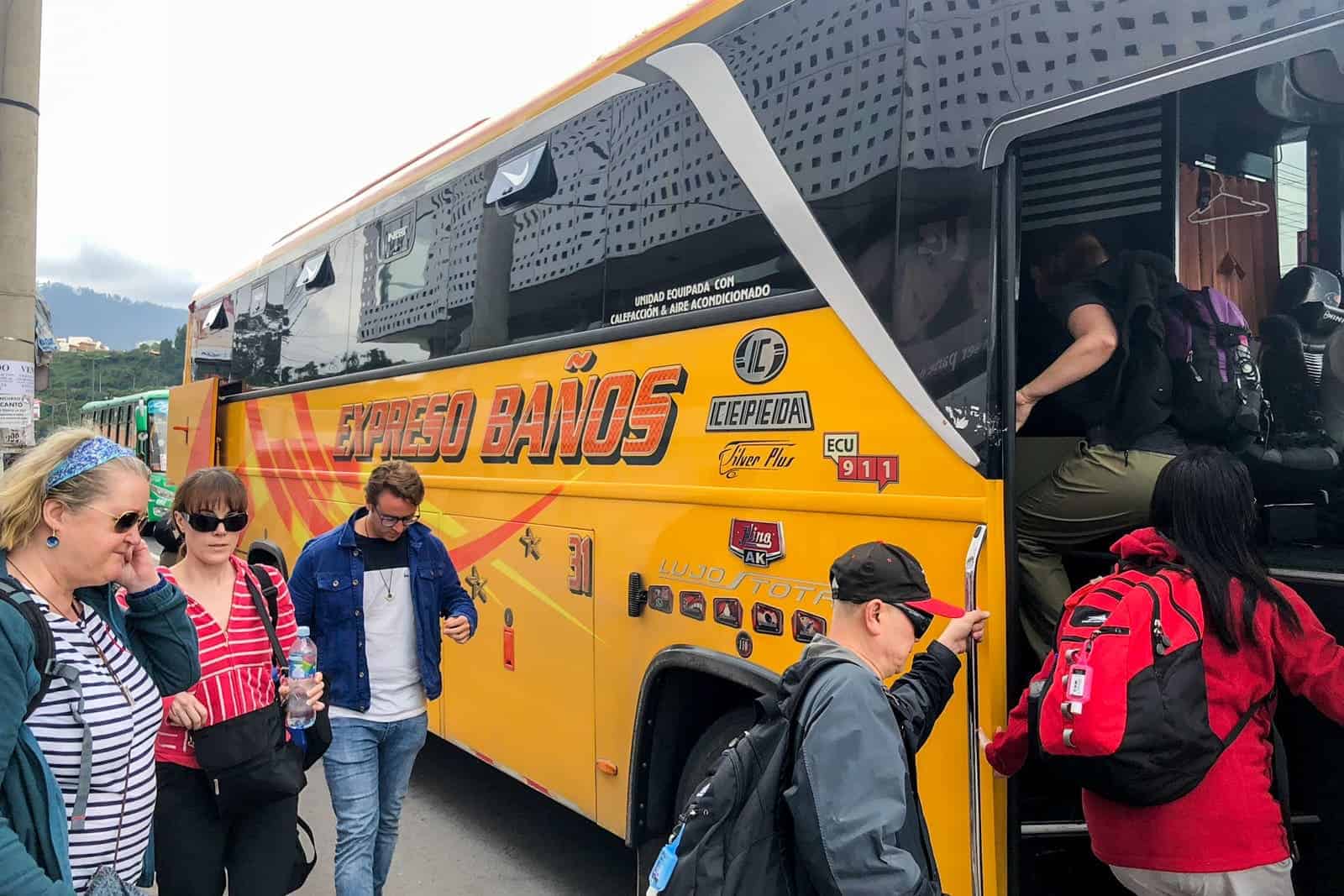 People board a yellow local bus Ecuador that reads 'Expreso Baños'. 