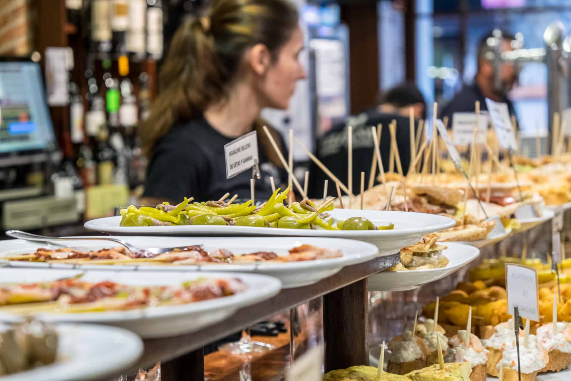 Pintxos - food with cocktail sticks - line white plates on two levels on a long bar in San Sebastian.