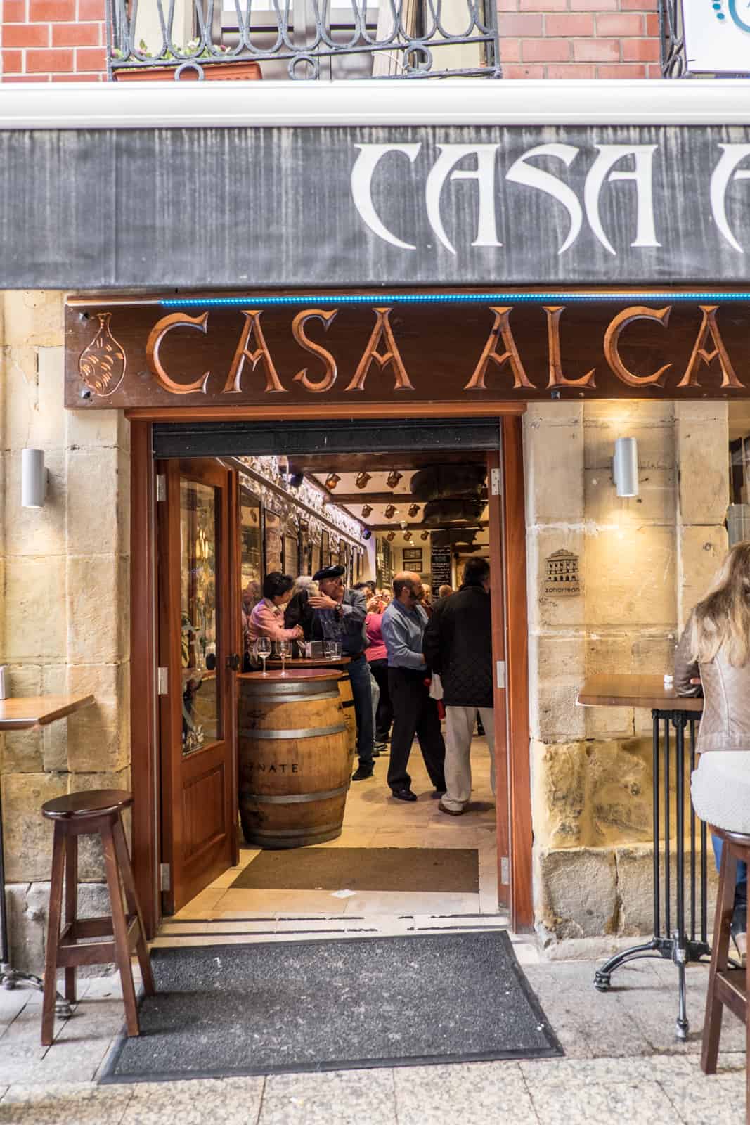 A brown wooden sign and doorway leading to the entrance of a busy Pintxos bar in San Sebastian.