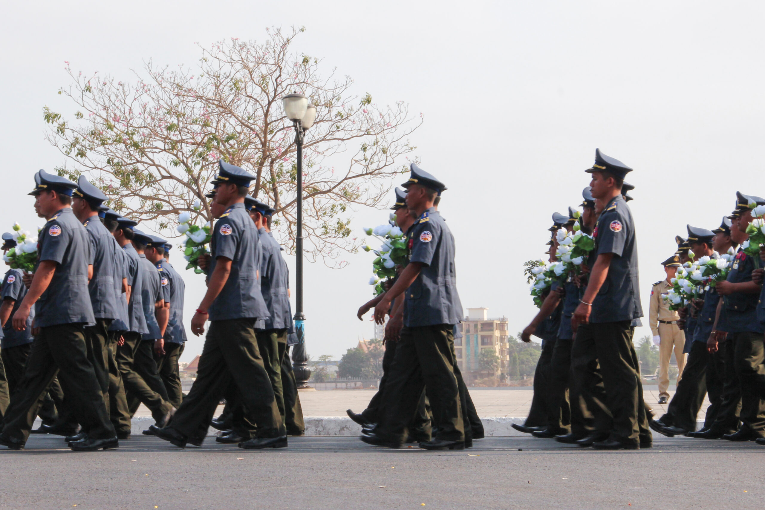 Cambodian forces dressed in dark blue shirts and army green trousers marching next to the Phnom Penh river in the parade of the funeral of the King Father.
