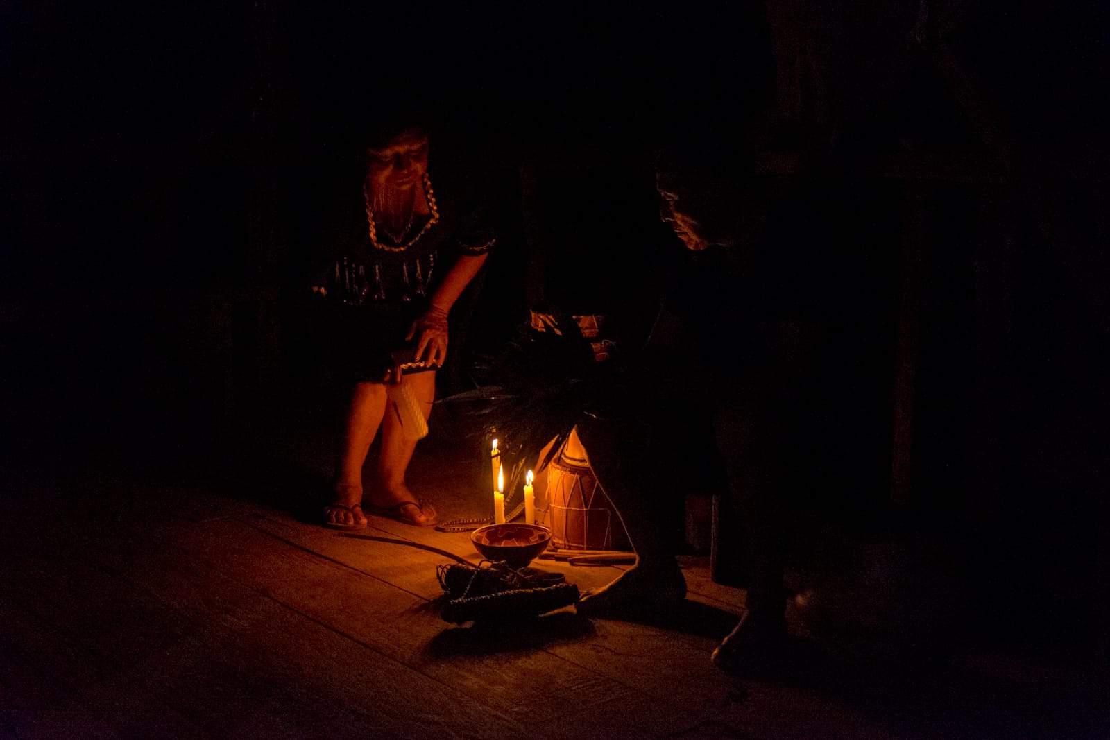 A man sits in the darkness with only candlelight as a woman leans over towards the light – Sharman practice in Ecuador Amazon Rainforest 