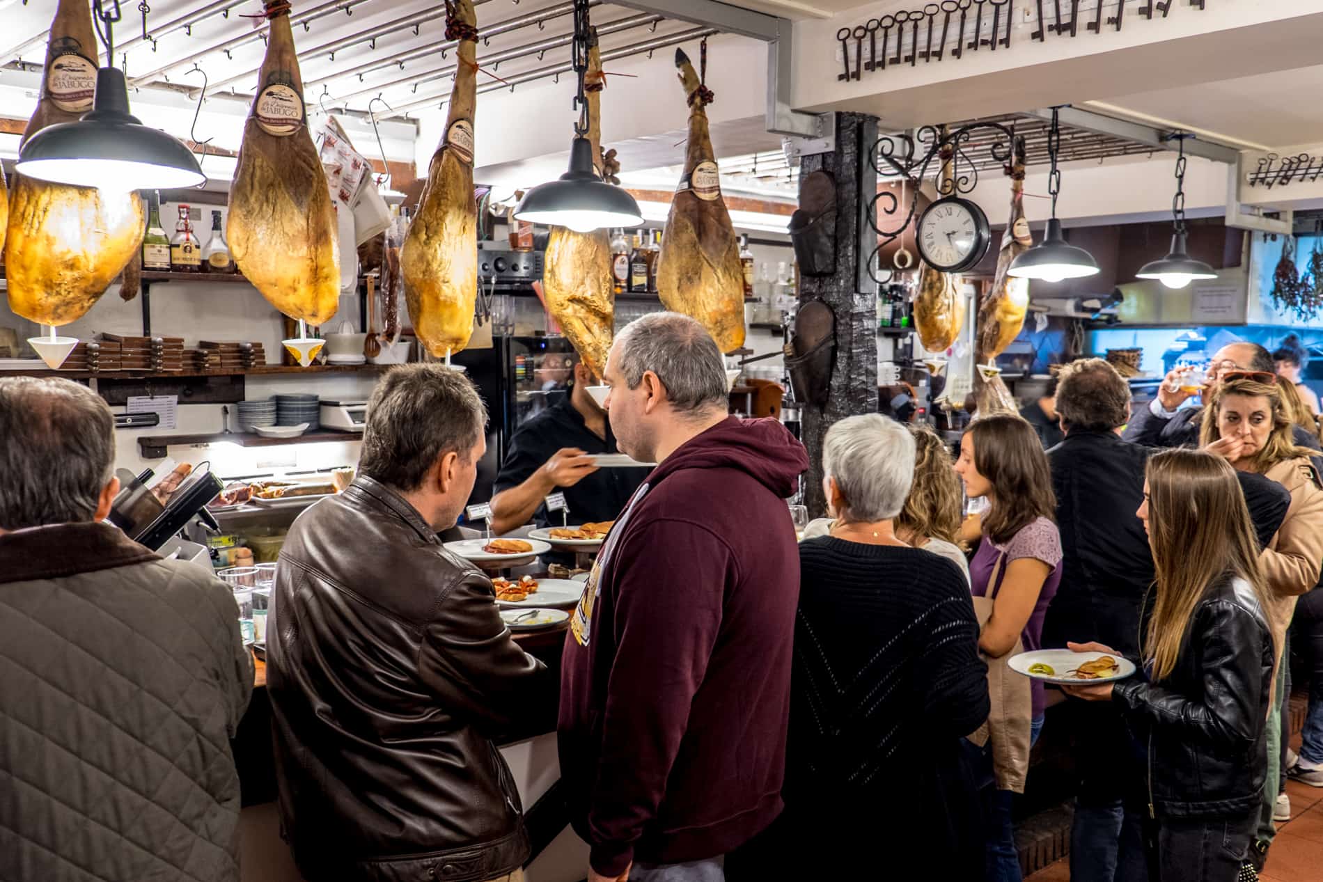 People sit and stand around a bar in San Sebastian underneath hanging legs of Jamon. 