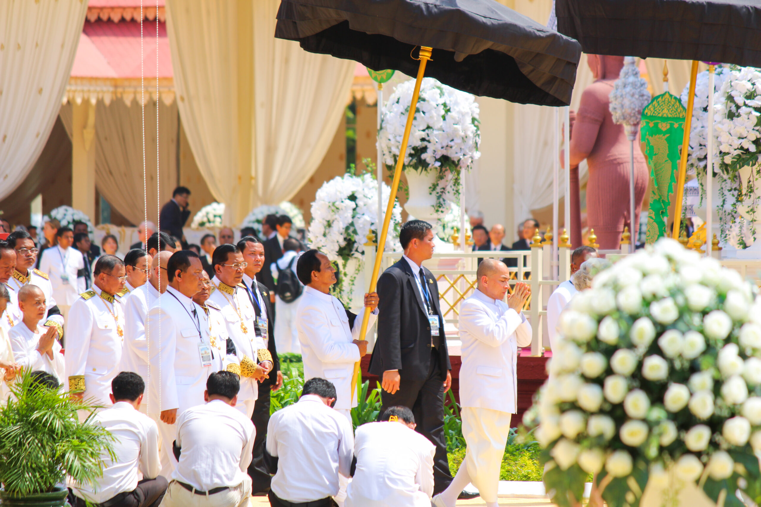 Close-up image of a group of delegates dressed in white, walking under a giant black umbrella during the funeral procession of Cambodia's former King Norodom Sihanouk.