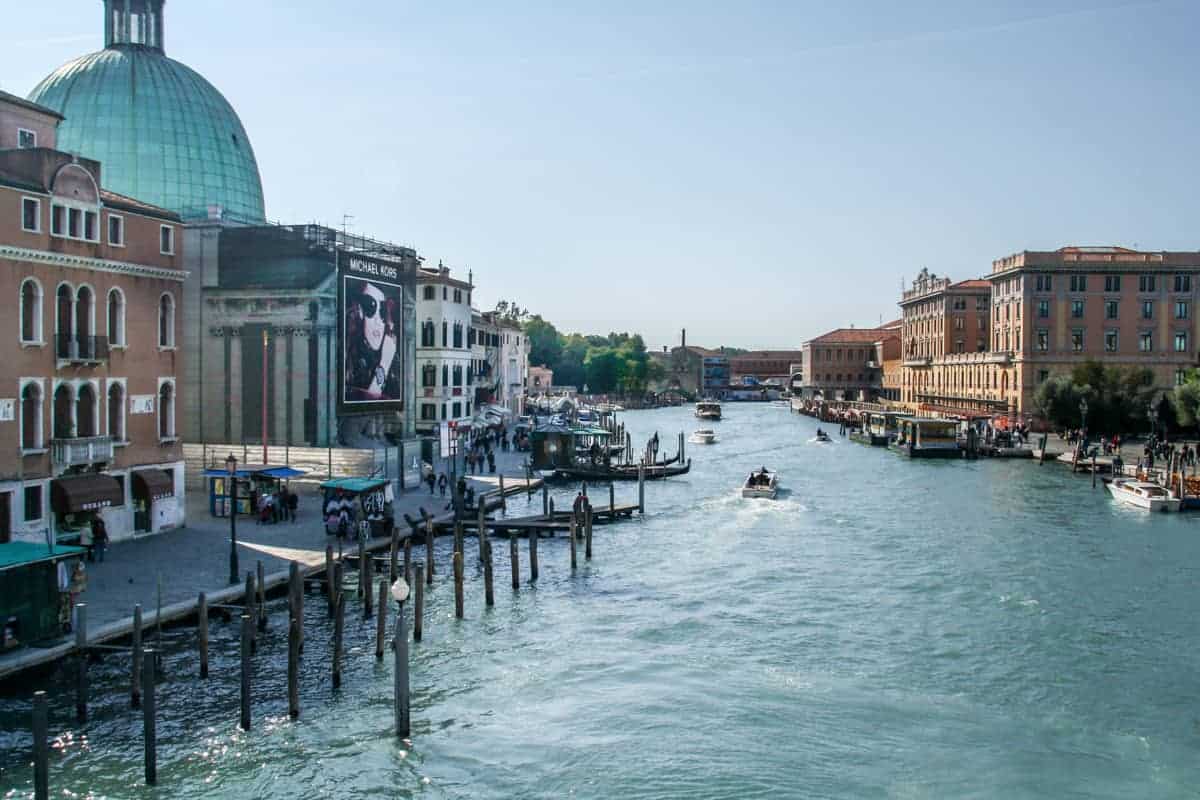 A view looking down part of the Venice Grand Canal, lined with public building and boat docks, while standing on one of the bridges