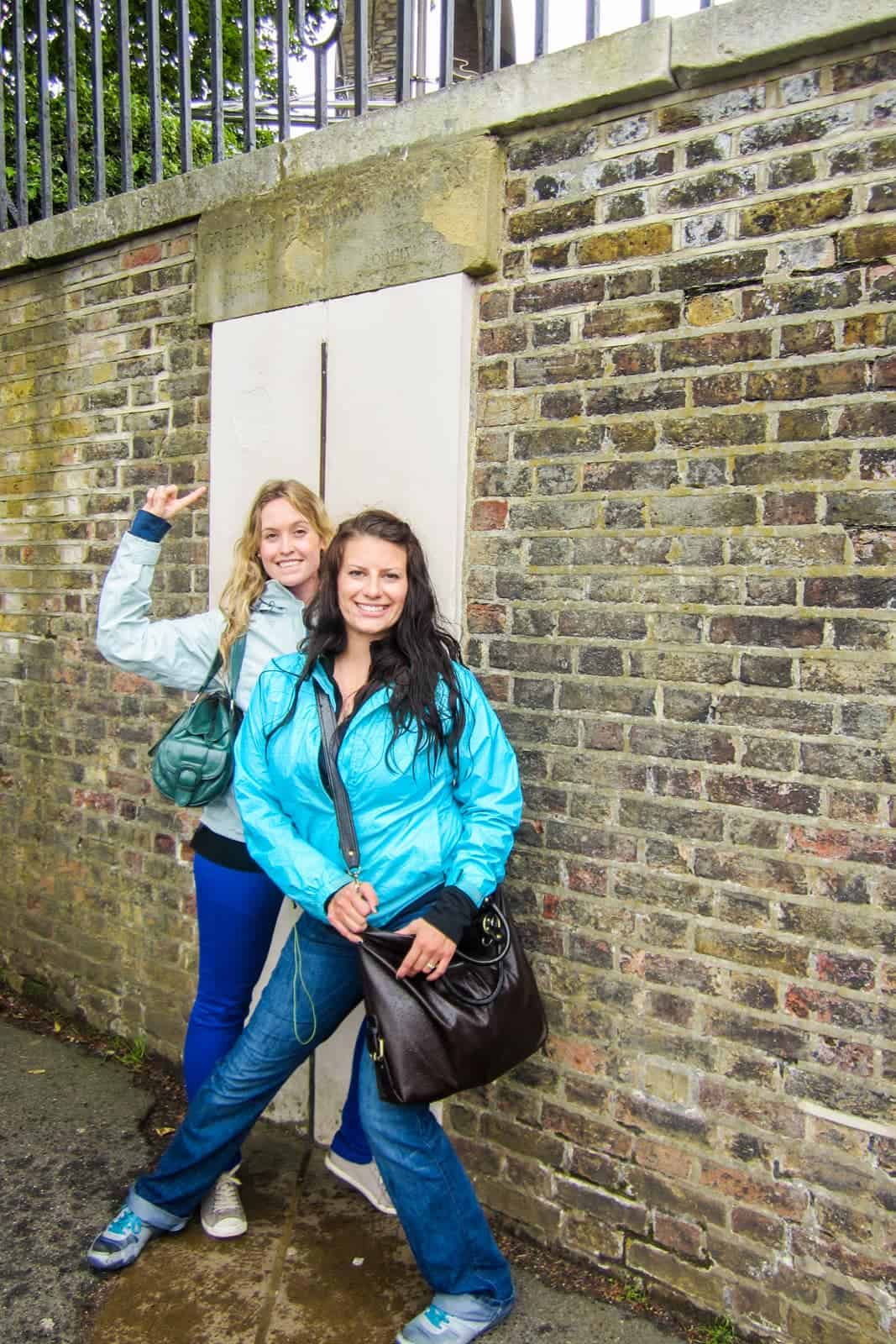 Two women standing at a wall displaying the Greenwich Mean Time Prime Meridian Line in London.