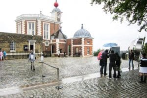 A small group of people standing on the Greenwich Prime Meridian Line in London in the rain.